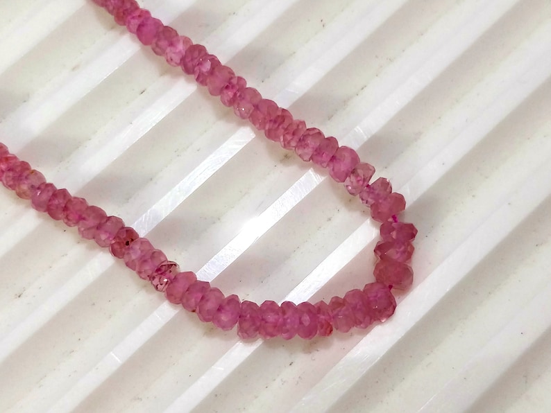 Pode incluir: Um fio de contas de pedras preciosas cor-de-rosa. As contas s&atilde;o facetadas e t&ecirc;m um formato ligeiramente irregular. As contas s&atilde;o enfiadas num fio transparente.