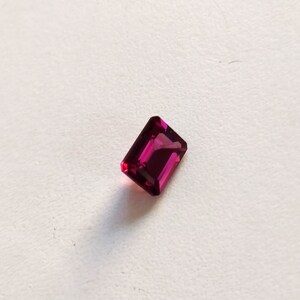 May include: A deep pink rectangular gemstone with a faceted cut.