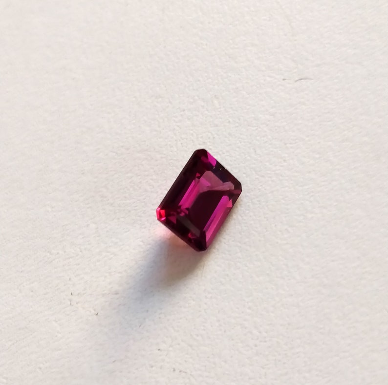 May include: A deep pink rectangular gemstone with a faceted cut.