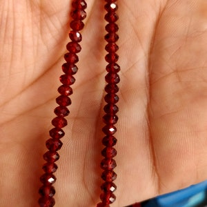 May include: A strand of dark red gemstone beads. The beads are faceted and have a shiny finish.