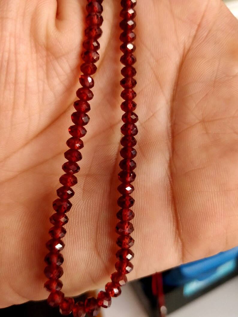 May include: A strand of dark red gemstone beads. The beads are faceted and have a shiny finish.