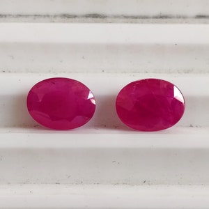 Puede incluir: Dos piedras preciosas ovaladas de color rosa brillante. Las piedras preciosas son lisas y pulidas.