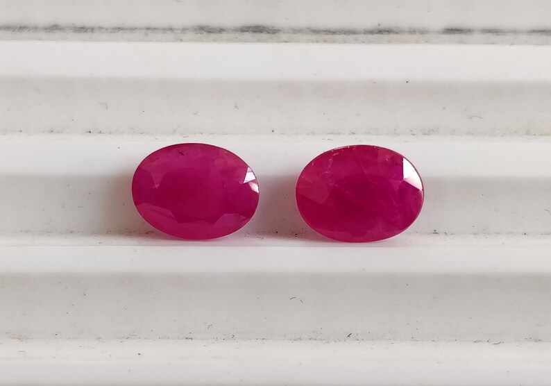 Puede incluir: Dos piedras preciosas ovaladas de color rosa brillante. Las piedras preciosas son lisas y pulidas.