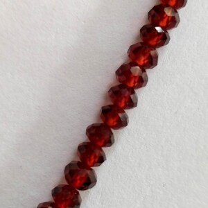 May include: A strand of dark red faceted beads. The beads are strung on a clear thread and are arranged in a straight line.