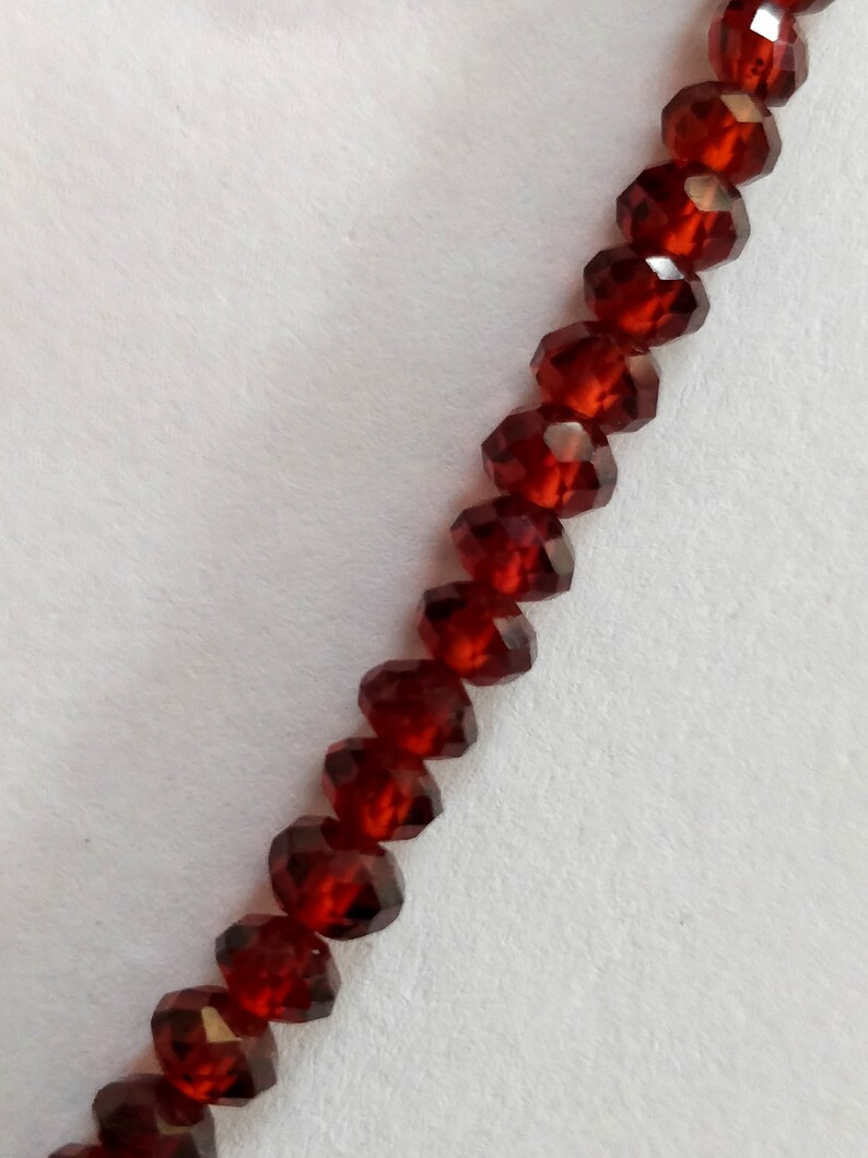 May include: A strand of dark red faceted beads. The beads are strung on a clear thread and are arranged in a straight line.