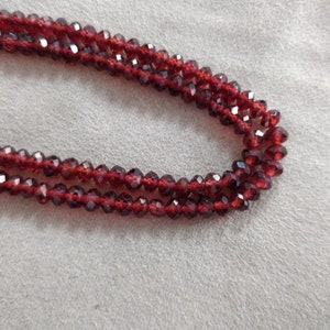 May include: A strand of red gemstone beads, likely garnet, with a faceted finish. The beads are strung on a clear thread and are arranged in a double row.