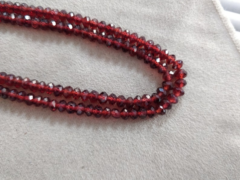 May include: A strand of red gemstone beads, likely garnet, with a faceted finish. The beads are strung on a clear thread and are arranged in a double row.
