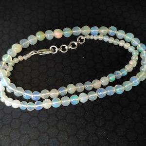 May include: A white opal beaded necklace with a silver clasp. The necklace is made of round, iridescent beads.