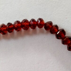 May include: A strand of dark red faceted glass beads. The beads are strung together on a clear thread.