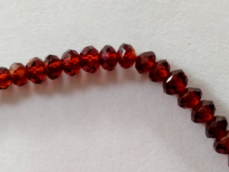 May include: A strand of dark red faceted glass beads. The beads are strung together on a clear thread.
