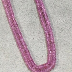Pode incluir: Um fio de contas de pedras preciosas cor-de-rosa, provavelmente safiras cor-de-rosa, enfiadas em um fio transparente. As contas s&atilde;o facetadas e t&ecirc;m uma forma ligeiramente irregular. O fio est&aacute; dobrado ao meio, criando um formato de U.