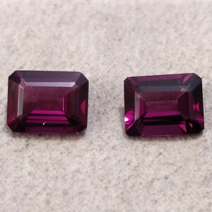 May include: Two purple rectangular gemstones with a faceted cut.