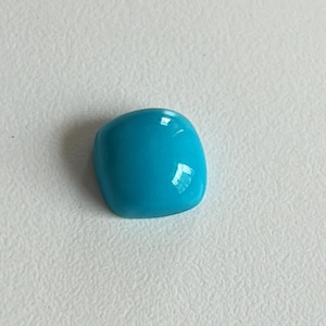 Pode incluir: Uma gema cabochão turquesa brilhante com uma superfície lisa e polida.