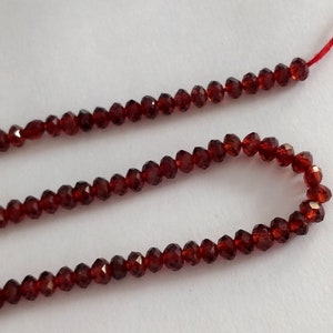 May include: A strand of red garnet beads, strung on a red thread. The beads are faceted and have a shiny finish.