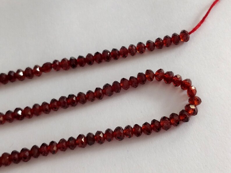 May include: A strand of red garnet beads, strung on a red thread. The beads are faceted and have a shiny finish.