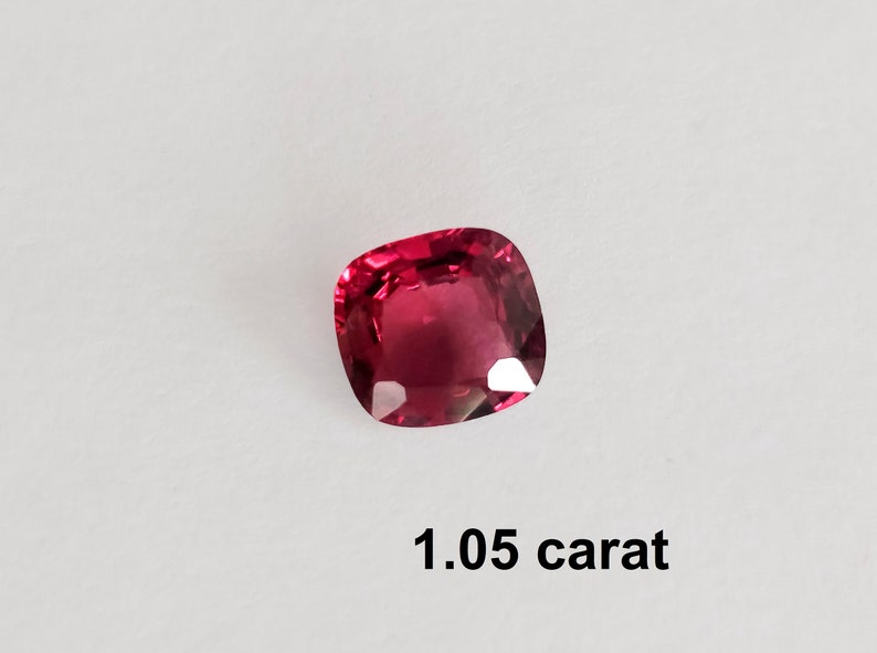 Pode incluir: Uma gema vermelha escura com corte almofada, pesando 1,05 quilates.