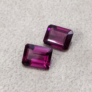 May include: Two purple rectangular gemstones with a faceted cut.