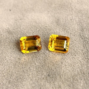 Op de afbeelding: Twee smaragd geslepen edelstenen, beide in een lichtgele kleur. De edelstenen liggen op een lichtgrijze achtergrond.