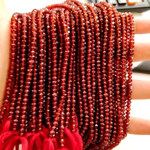 May include: A strand of red faceted garnet beads. The beads are small and uniform in size. The strand is tied with red string.