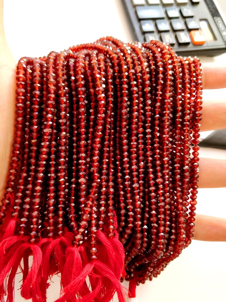 May include: A strand of red faceted garnet beads. The beads are small and uniform in size. The strand is tied with red string.
