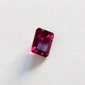 May include: A deep red gemstone with a rectangular emerald cut.