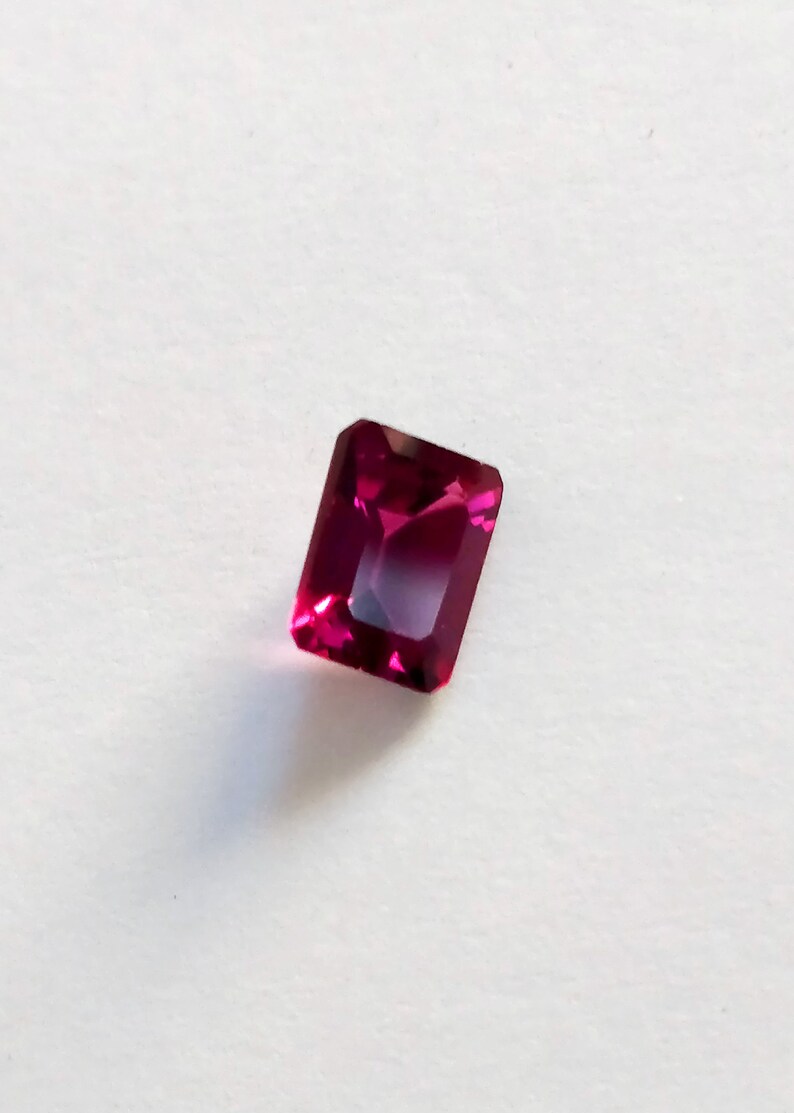 May include: A deep red gemstone with a rectangular emerald cut.