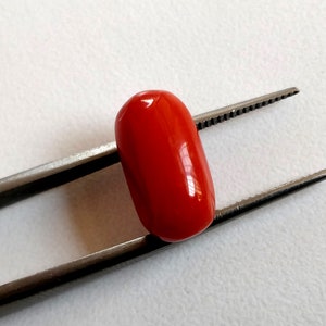May include: A bright red oval-shaped coral gemstone held in tweezers.