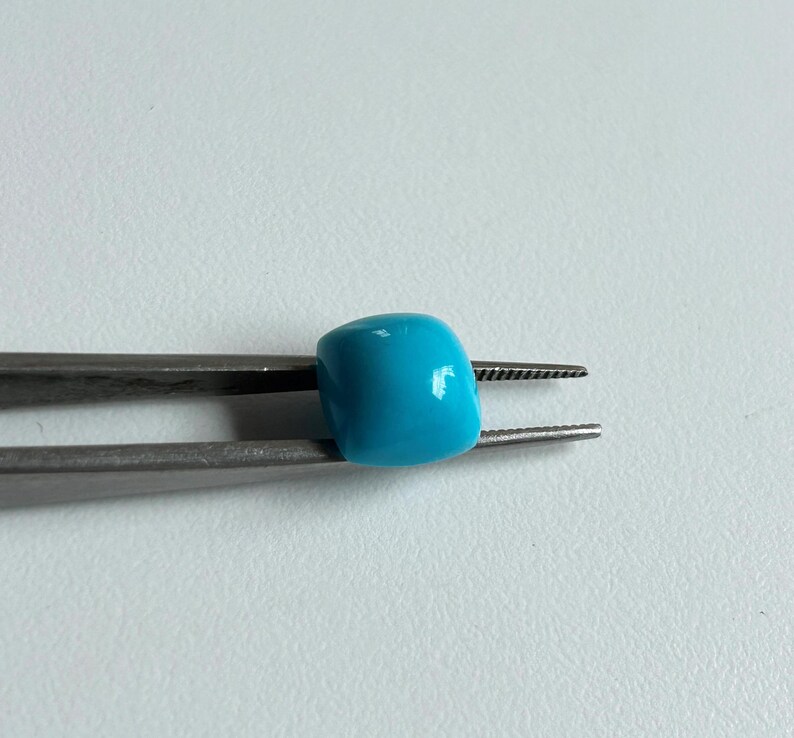 May include: A turquoise blue bead held in silver tweezers. The bead is round and smooth.