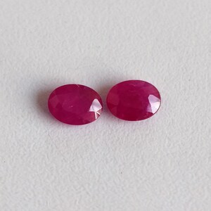 Puede incluir: Dos piedras preciosas de rub&iacute; de forma ovalada, cada una con un color rojo intenso y una superficie lisa y pulida.
