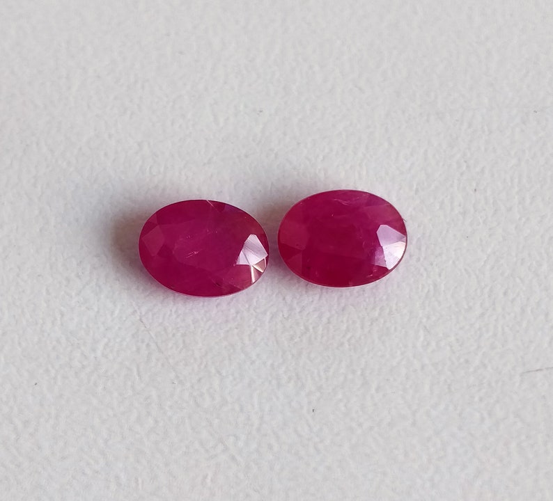 Puede incluir: Dos piedras preciosas de rub&iacute; de forma ovalada, cada una con un color rojo intenso y una superficie lisa y pulida.