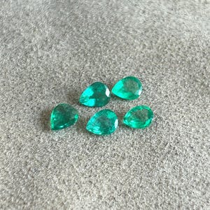K&ouml;nnte beinhalten: F&uuml;nf lose, birnenf&ouml;rmige Edelsteine in einer leuchtenden, durchscheinenden gr&uuml;nen Farbe. Jeder Stein weist eine facettierte Oberfl&auml;che auf, die das Licht reflektiert und f&uuml;r ein funkelndes Aussehen sorgt. Die Edelsteine sind in einer Gruppe angeordnet.