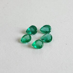 K&ouml;nnte beinhalten: F&uuml;nf lose, birnenf&ouml;rmige Smaragd-Edelsteine mit leuchtend gr&uuml;ner Farbe und facettierten Oberfl&auml;chen. Jeder Stein weist eine klare, durchscheinende Qualit&auml;t mit nat&uuml;rlichen Einschl&uuml;ssen auf und ist in einer Gruppe auf einer hellen Fl&auml;che angeordnet.