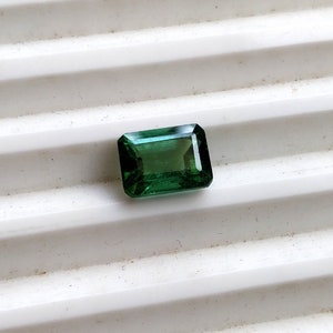 May include: A green emerald gemstone cut into a rectangular shape.