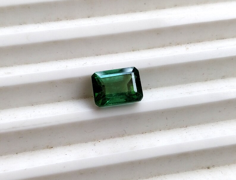 May include: A green emerald gemstone cut into a rectangular shape.