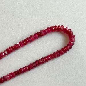 May include: A strand of faceted, deep red ruby beads. The beads are small and uniform in size, strung together to form a necklace or bracelet. The gemstones have a rich, saturated color.