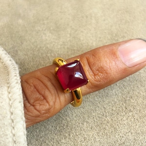 May include: A gold ring with a square, red gemstone.