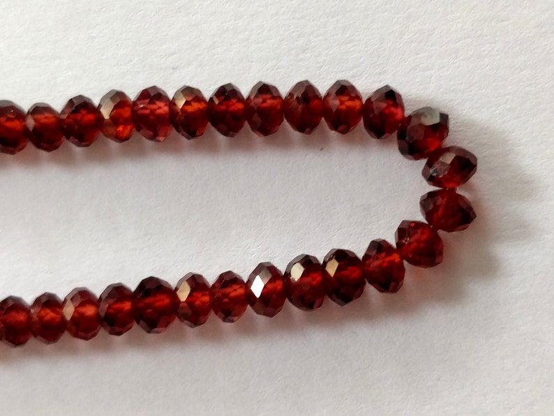 May include: A strand of dark red faceted gemstone beads. The beads are small and round, and they are strung on a clear thread.