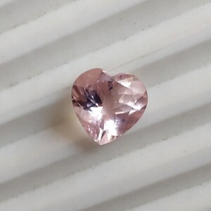 Op de afbeelding: Een roze edelsteen in de vorm van een hart met facetten.