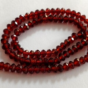 May include: A strand of deep red faceted garnet beads. The beads are strung on a clear thread and are approximately 4mm in diameter.