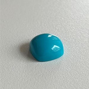 May include: A bright turquoise cabochon gemstone, cut and polished, with a smooth, rounded surface.