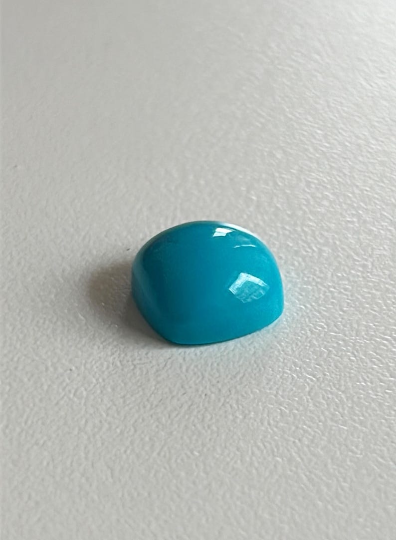 May include: A bright turquoise cabochon gemstone, cut and polished, with a smooth, rounded surface.