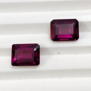 May include: Two purple rectangular gemstones with a faceted cut.