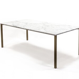 Puede incluir: Una mesa de comedor rectangular con una tapa de m&aacute;rmol blanco y un marco de lat&oacute;n. La mesa tiene un dise&ntilde;o simple y moderno.