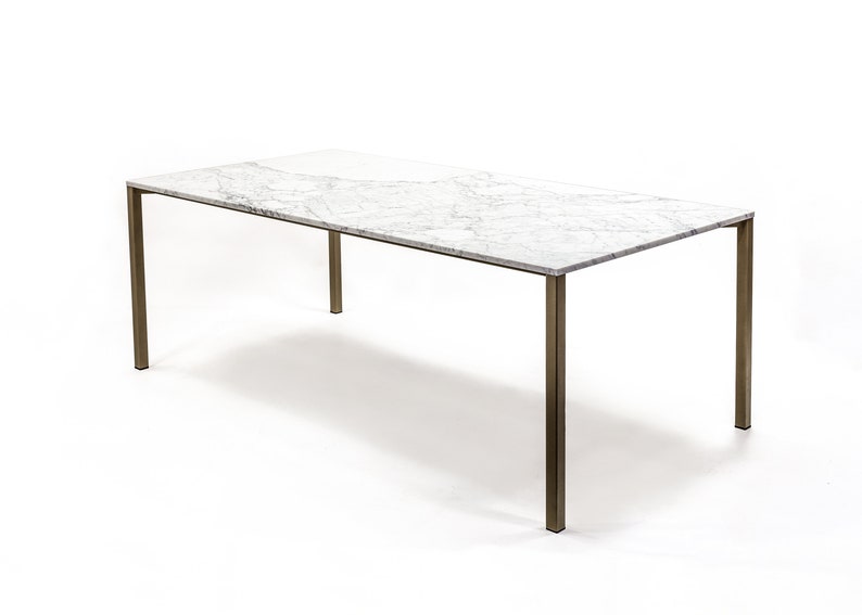 Puede incluir: Una mesa de comedor rectangular con una tapa de m&aacute;rmol blanco y un marco de lat&oacute;n. La mesa tiene un dise&ntilde;o simple y moderno.