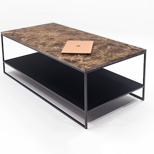 Peut inclure: Une table basse rectangulaire avec un plateau en marbre brun et une étagère inférieure noire. La table a un cadre en métal noir et est posée sur une surface blanche.