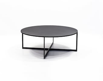 May include: A black round coffee table with a simple, modern design. The table has a black metal frame with a cross-shaped base and a round black tabletop.