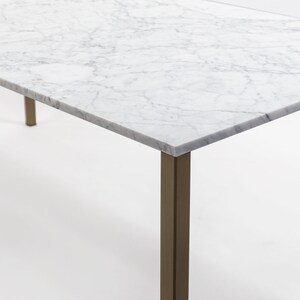Puede incluir: Una mesa con tapa de m&aacute;rmol blanco y base de metal dorado. La tapa de la mesa tiene un patr&oacute;n veteado natural.