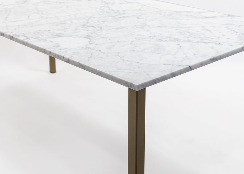 Puede incluir: Una mesa con tapa de m&aacute;rmol blanco y base de metal dorado. La tapa de la mesa tiene un patr&oacute;n veteado natural.