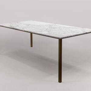 Puede incluir: Una mesa de comedor rectangular con una tapa de m&aacute;rmol blanco y un marco de lat&oacute;n. La mesa tiene un dise&ntilde;o simple y moderno.