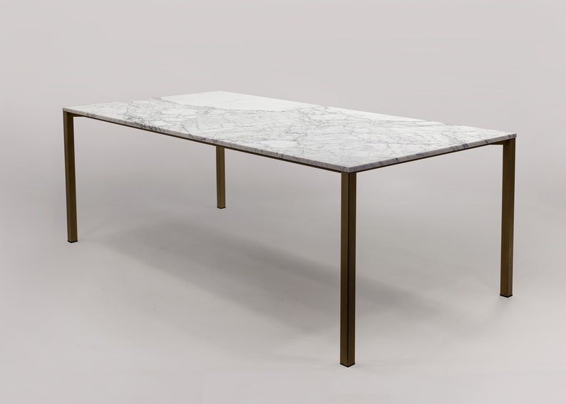 Puede incluir: Una mesa de comedor rectangular con una tapa de m&aacute;rmol blanco y un marco de lat&oacute;n. La mesa tiene un dise&ntilde;o simple y moderno.